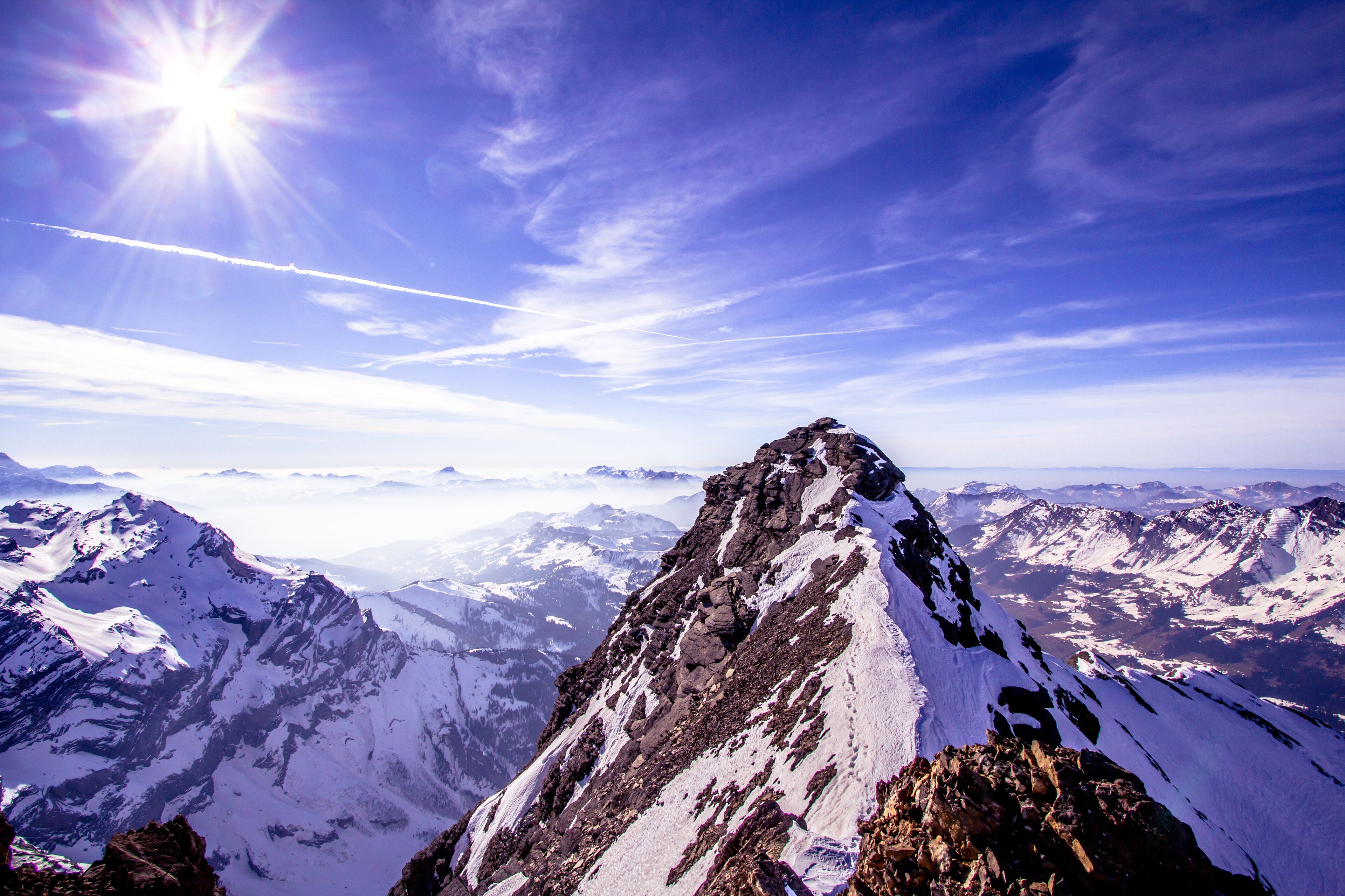 A snow-covered mountain peak with a clear sky and distant mountain ranges.