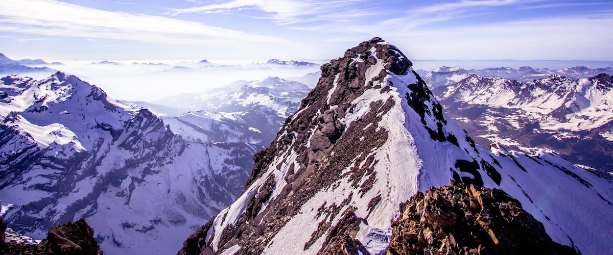 A snow-covered mountain peak with a clear sky and distant mountain ranges.