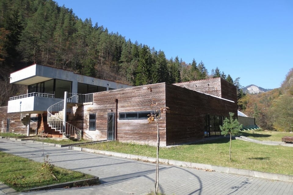 A modern building with a wooden facade, a spiral staircase, and a view of a forested hillside.