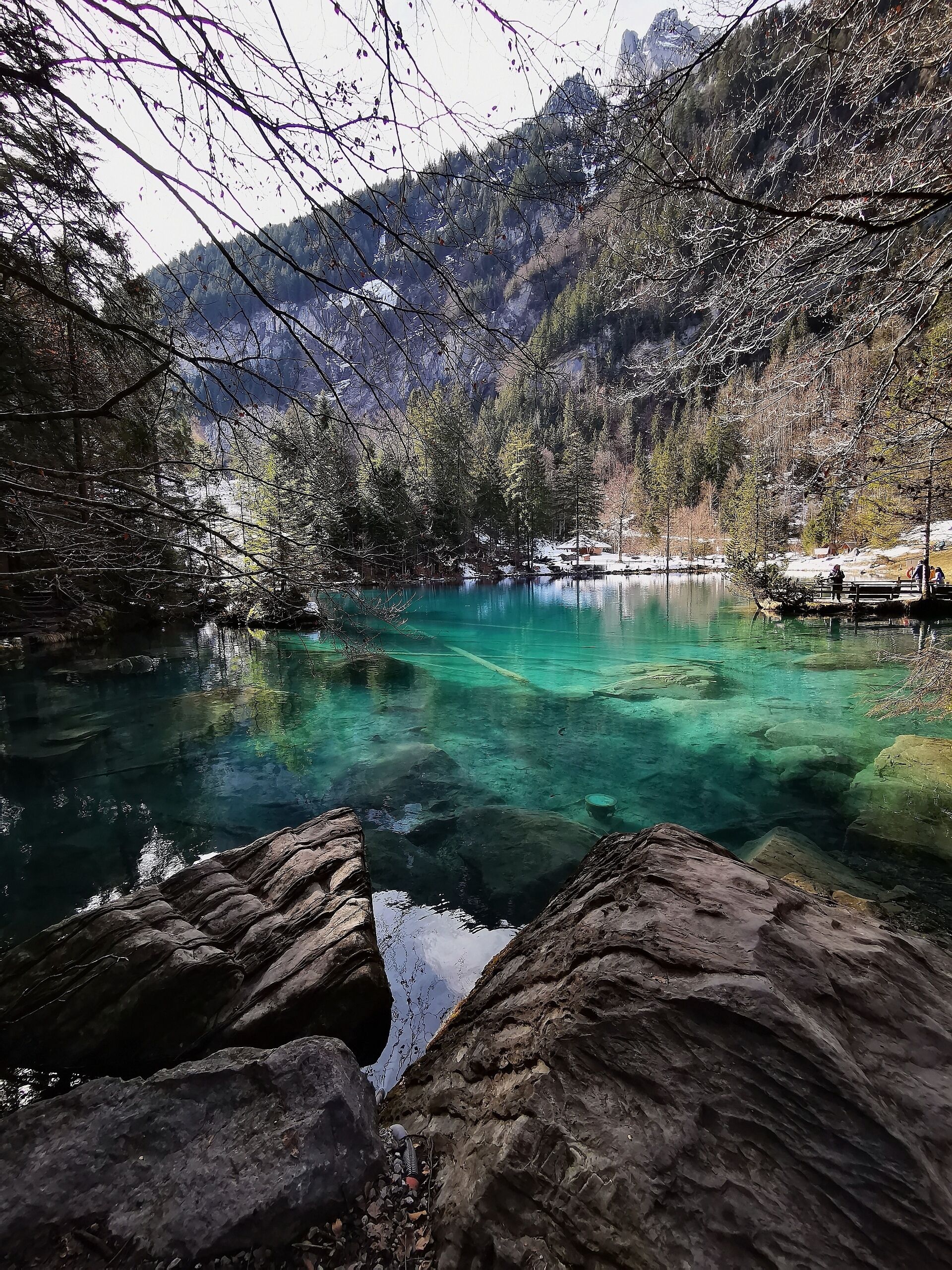 A clear mountain lake surrounded by trees and rocky terrain.