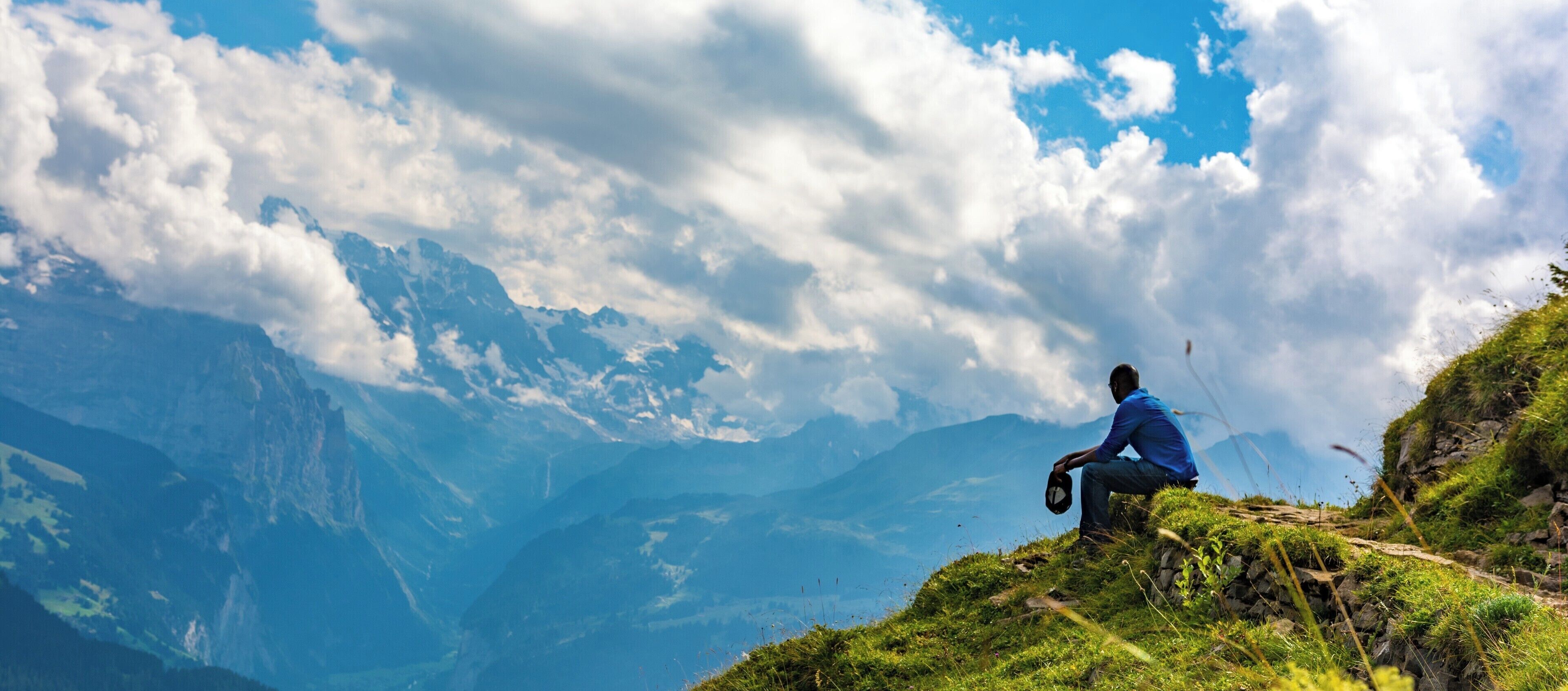 A person sitting on a grassy hill with a mountain range in the background.