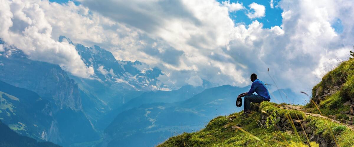 A person sitting on a grassy hill with a mountain range in the background.