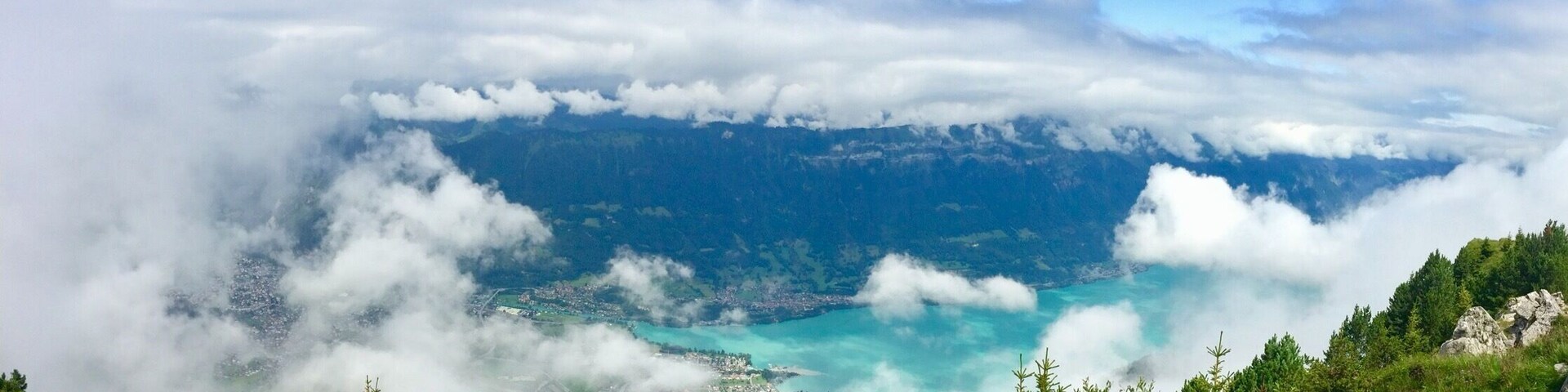 Paisaje montañoso con un lago turquesa rodeado de nubes y vegetación.