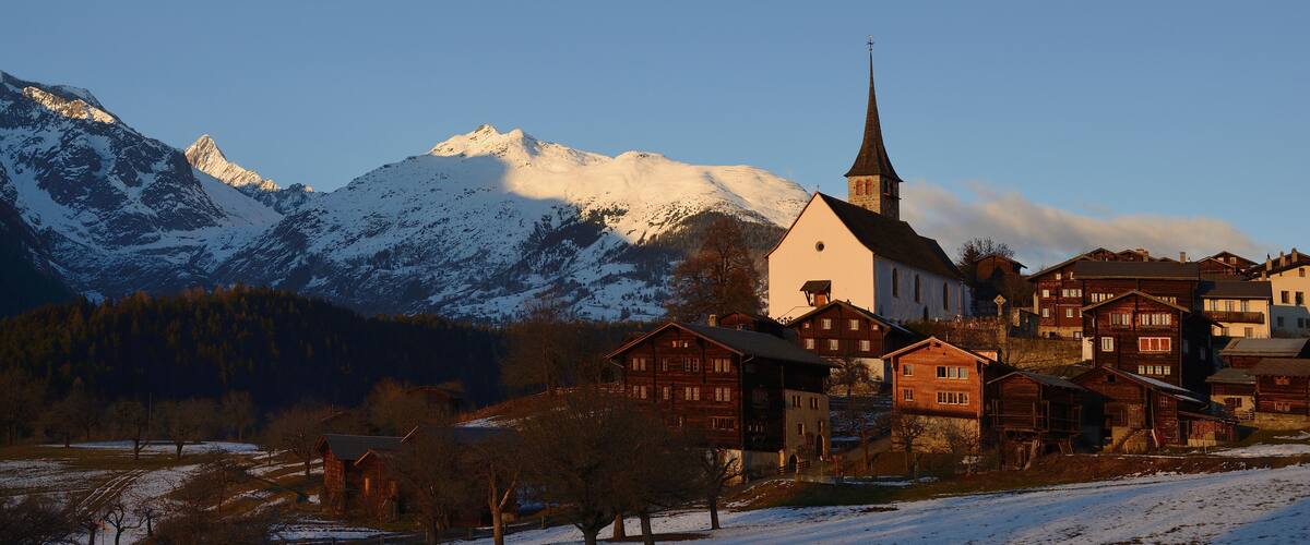 A snow-covered mountain range with a church and traditional buildings in a valley.