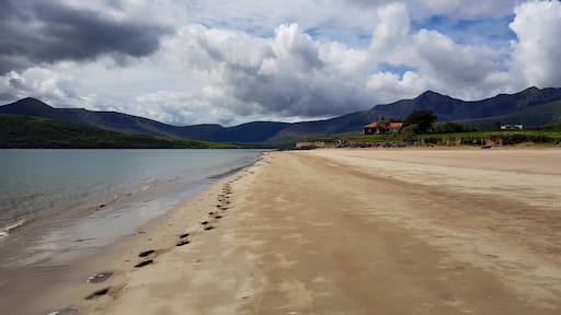 Footprints in the sand along seaside beach with building and mountains, cloudy sky. Cappagh Beach, Cloghane-Brandon, County Kerry, Ireland