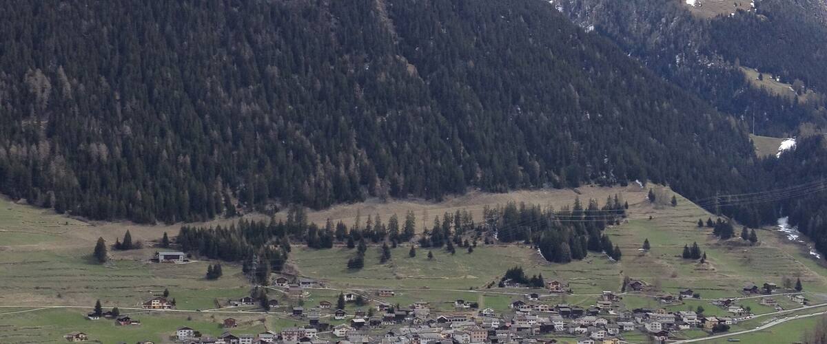 A small village nestled in a valley surrounded by dense forests and mountains.