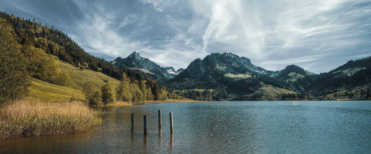 A calm lake surrounded by forested hills and mountains under a cloudy sky.
