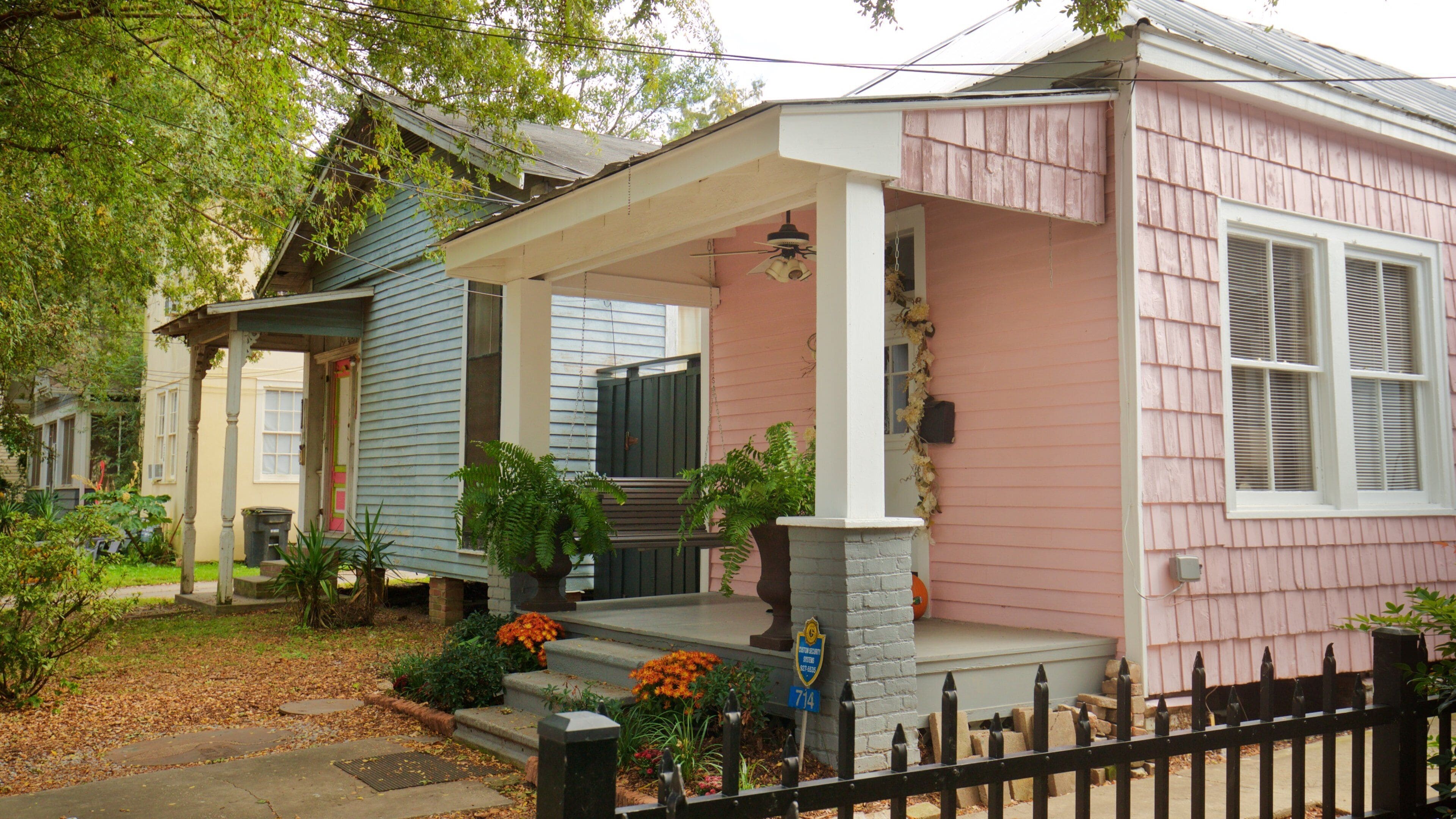A pink house with a porch, a blue house next to it, and a black fence.