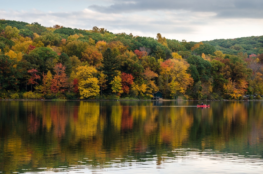 Lonely Canoe on a Mountain Lake with Wooded Shores in Autumn. Great Reflection in Water
