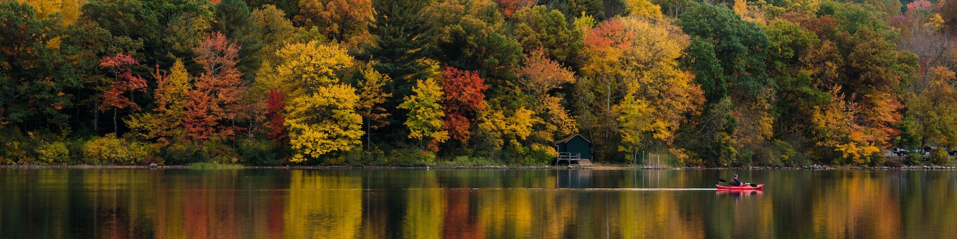 Lonely Canoe on a Mountain Lake with Wooded Shores in Autumn. Great Reflection in Water