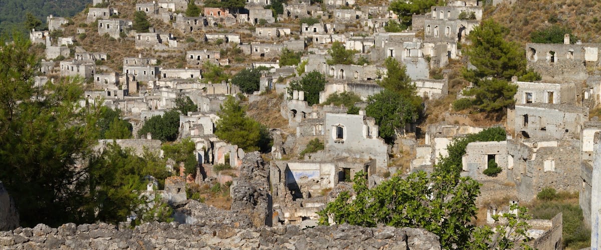 A hillside settlement with numerous stone buildings, some with visible windows and doors, surrounded by trees and rocky terrain.