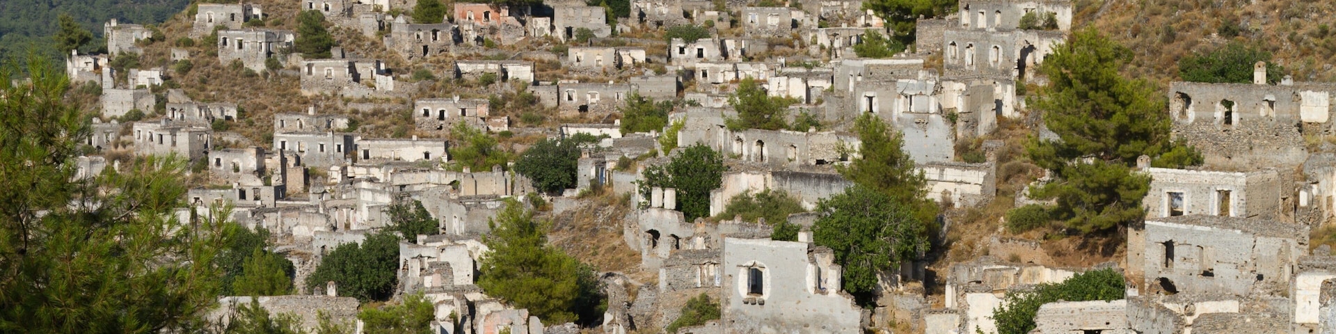 A hillside settlement with numerous stone buildings, some with visible windows and doors, surrounded by trees and rocky terrain.