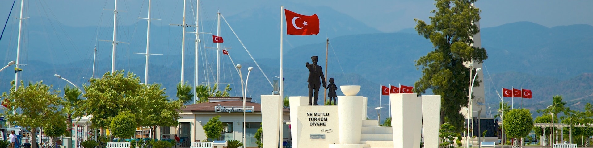 Um monumento com uma bandeira, uma estátua e um edifício com uma placa.