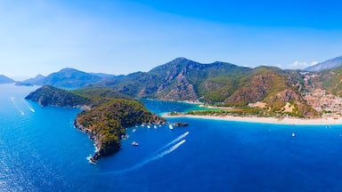 A coastal landscape with a beach, clear blue waters, and mountainous terrain.