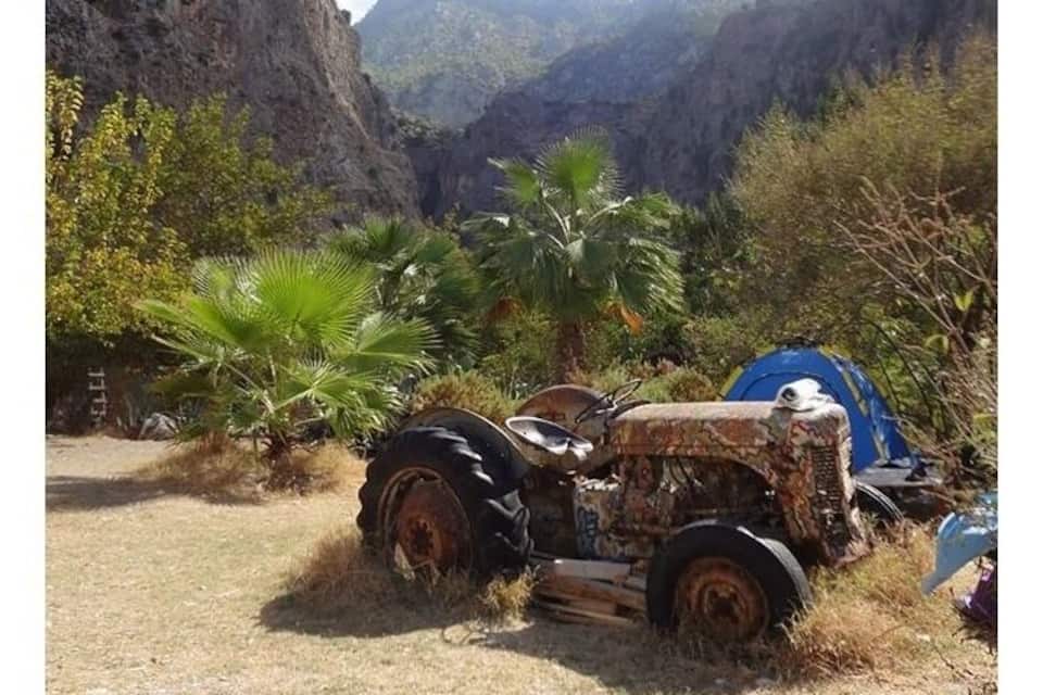 An abandoned vehicle in a dry, mountainous area with sparse vegetation.