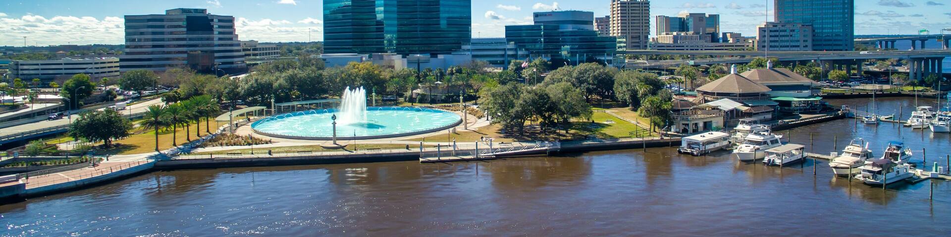 A marina with boats, a fountain, and modern buildings in the background.
