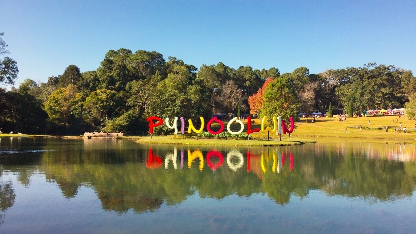 A lake with colorful letters spelling 'PUINOESLA' on the shore, surrounded by trees and a clear sky.