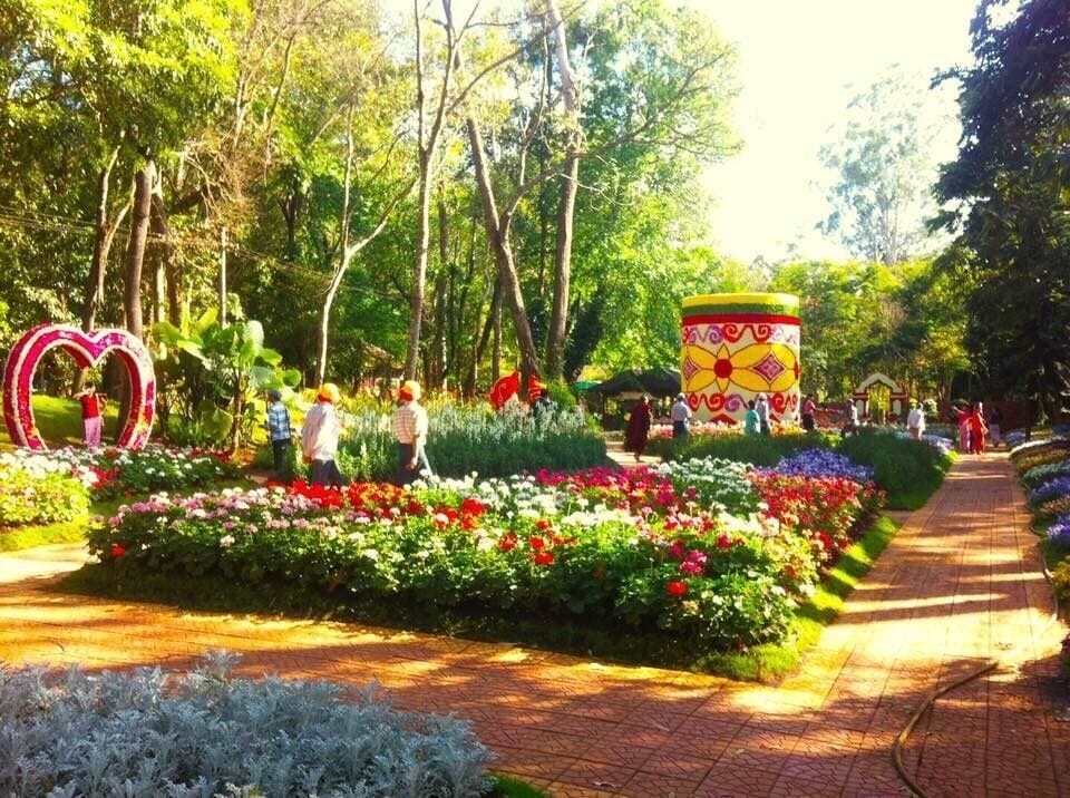 Un jardín con una escultura con forma de corazón, una estructura cilíndrica colorida y un sendero bordeado de flores.