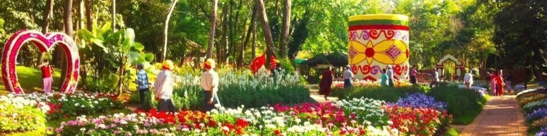 Un jardín con una escultura con forma de corazón, una estructura cilíndrica colorida y un sendero bordeado de flores.
