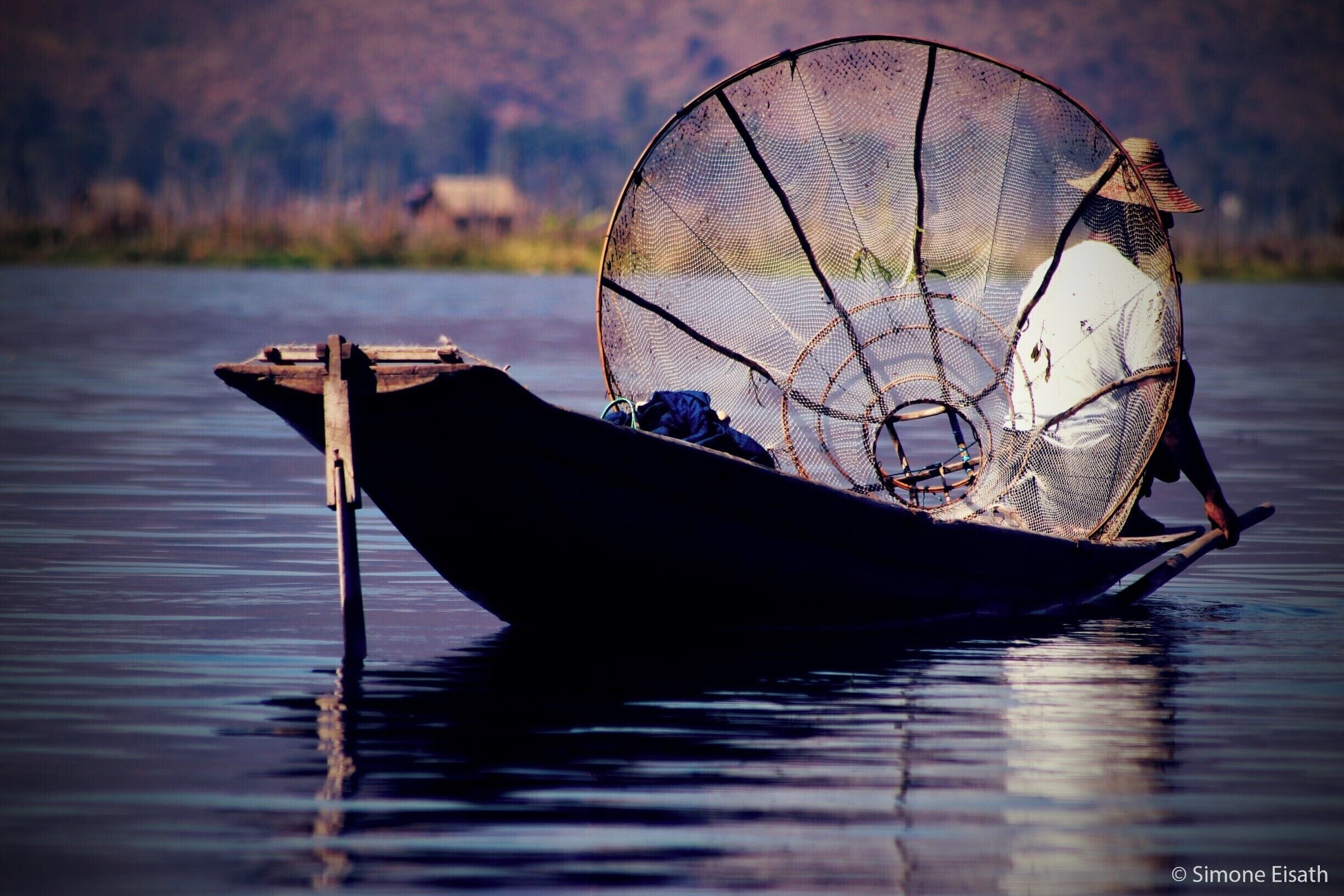 Un bote tradicional con una gran red de pesca sobre aguas tranquilas.