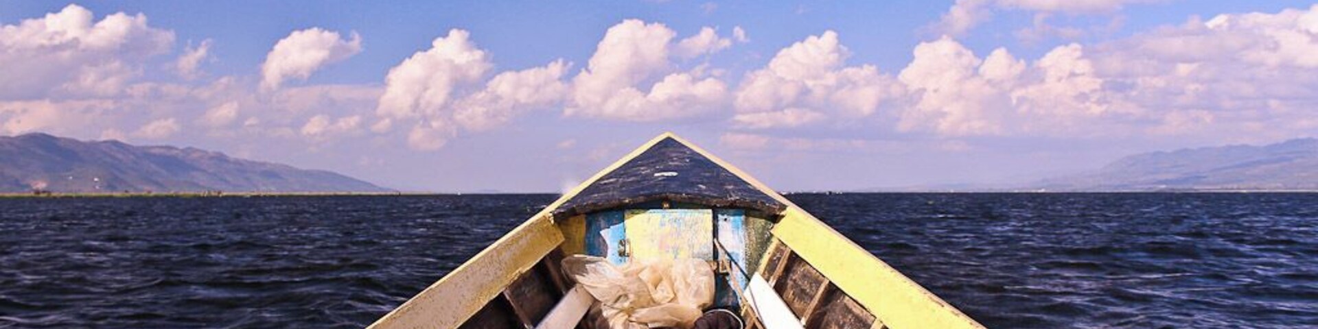 A wooden boat on a calm body of water with mountains in the background.