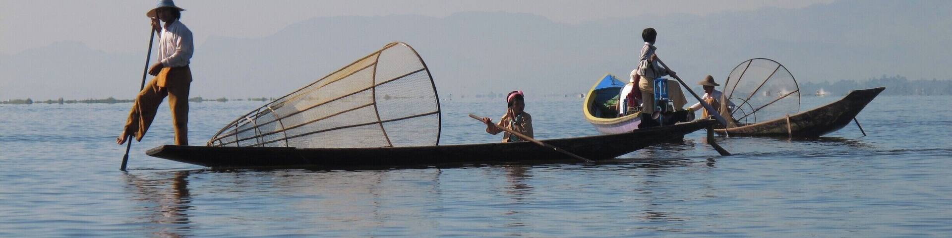 Three traditional boats on a calm body of water with mountains in the background.