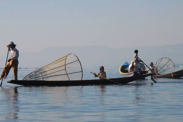 Three traditional boats on a calm body of water with mountains in the background.