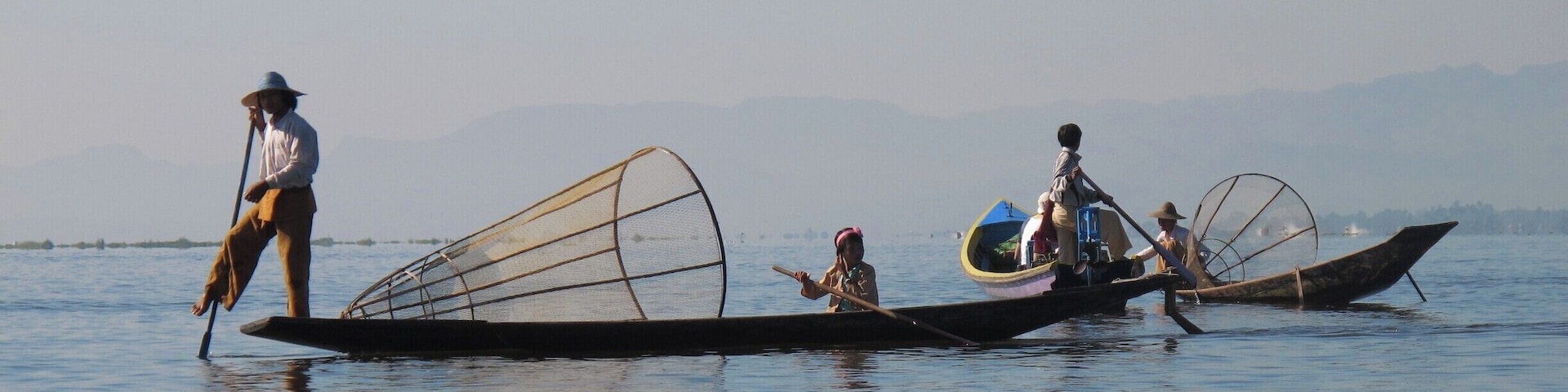 Três barcos tradicionais em águas calmas, com montanhas ao fundo.