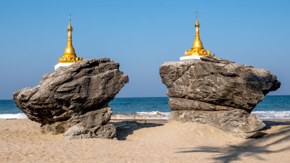 Two golden pagodas on large rocks by the sea.