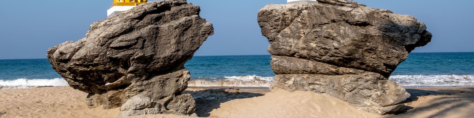 Two golden pagodas on large rocks by the sea.