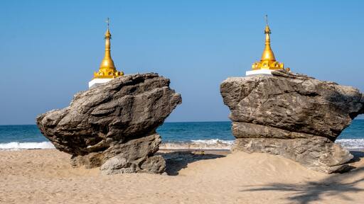 Two golden pagodas on large rocks by the sea.