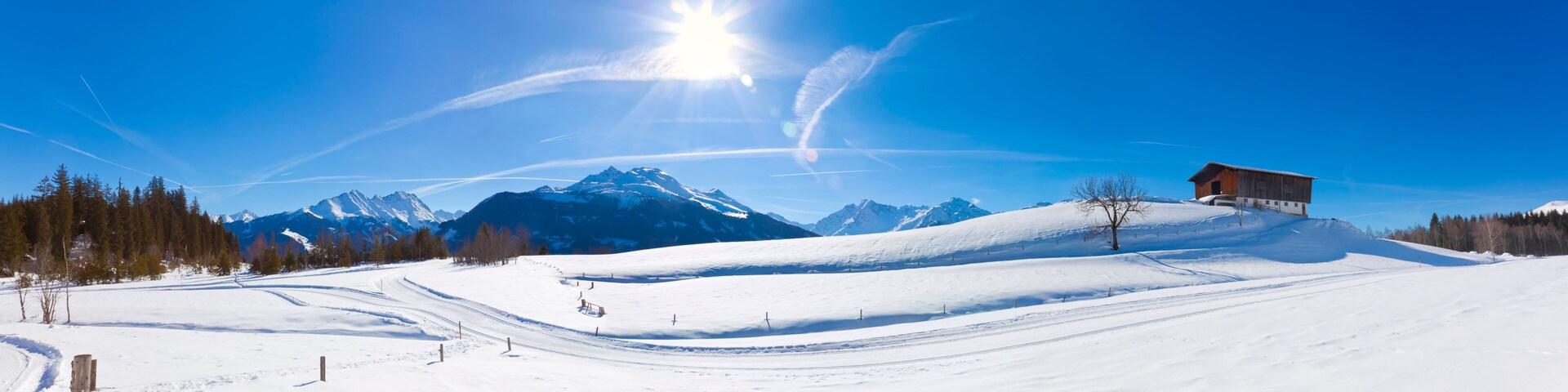 Pista de esquí nevada con una cabaña de madera, un telesilla y una cordillera bajo un cielo azul despejado.