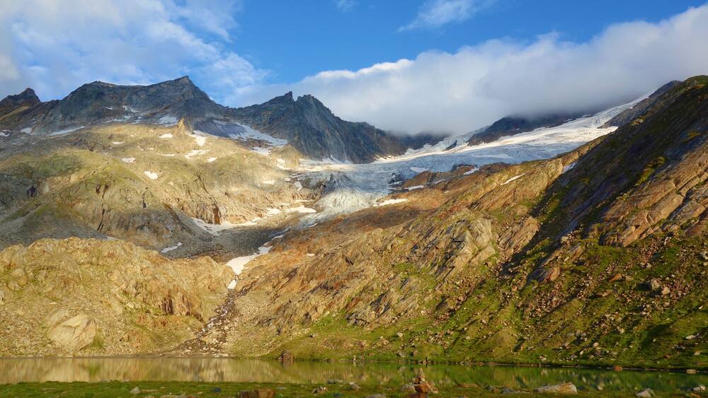 Eine Berglandschaft mit Gletscher, felsigem Gelände und einem See.