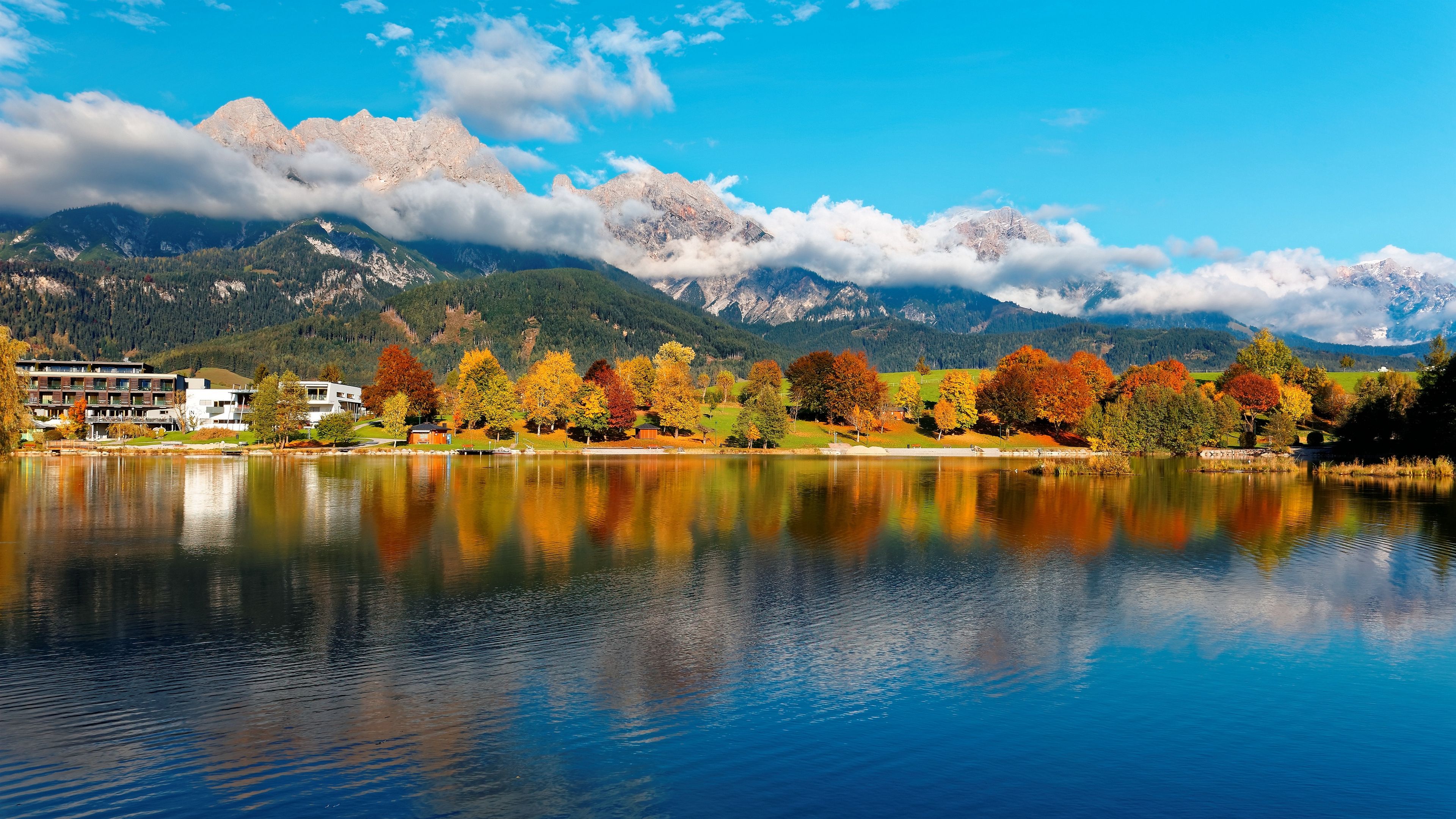 Scenery of beautiful Lake Ritzensee on a sunny autumn day in Saalfelden, Salzburger Land, Austria, with reflections of colorful fall foliage on the peaceful lake & majestic Austrian Alps in background