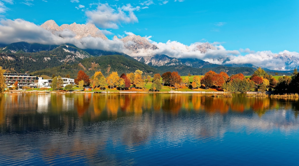 Ein ruhiger See, der Herbstbäume und Berge spiegelt.