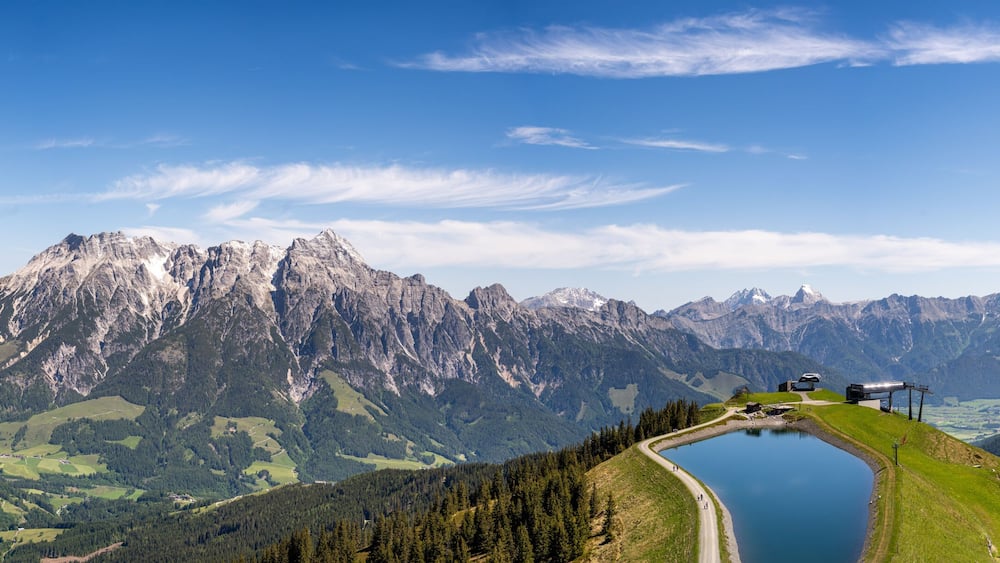 A mountain landscape with a lake, a road, and a building on the right.