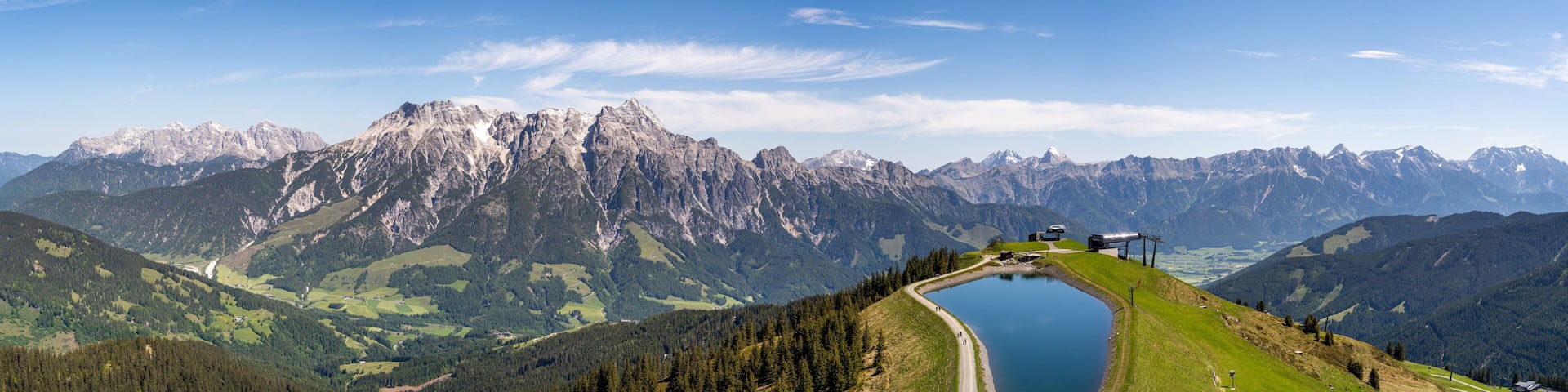 A mountain landscape with a lake, a road, and a building on the right.