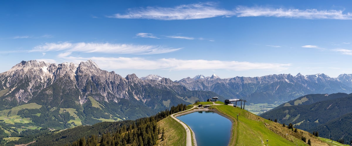 A mountain landscape with a lake, a road, and a building on the right.