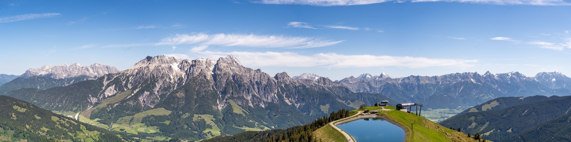 A mountain landscape with a lake, a road, and a building on the right.