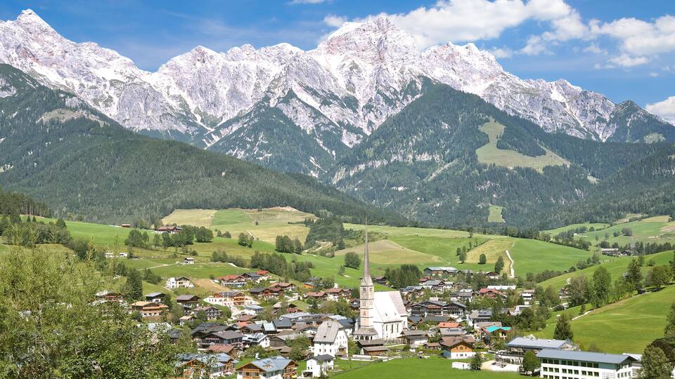 A mountain village with snow-capped peaks, a church, and lush green fields.