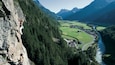 Un alpiniste sur une paroi rocheuse escarpée, avec une vallée et une rivière en contrebas.