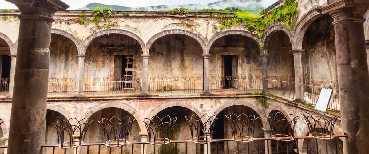 An ancient stone courtyard with arches and columns, surrounded by a metal fence.