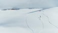 Een besneeuwde berg met twee skiërs die een helling afdalen.
