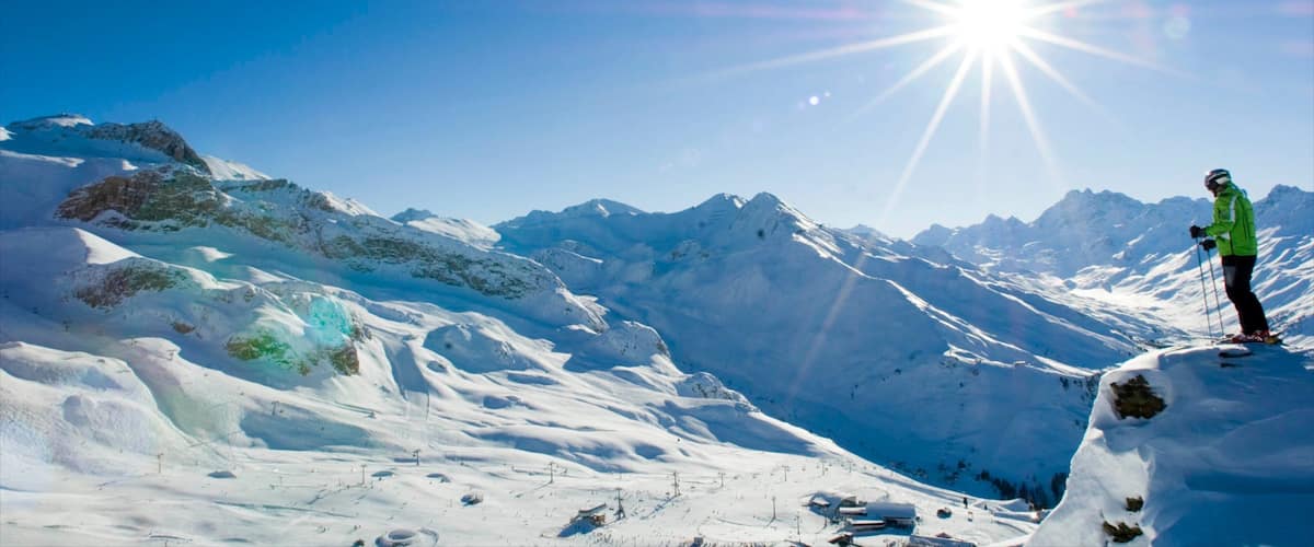 A skier on a snowy mountain with a clear sky and sun shining.