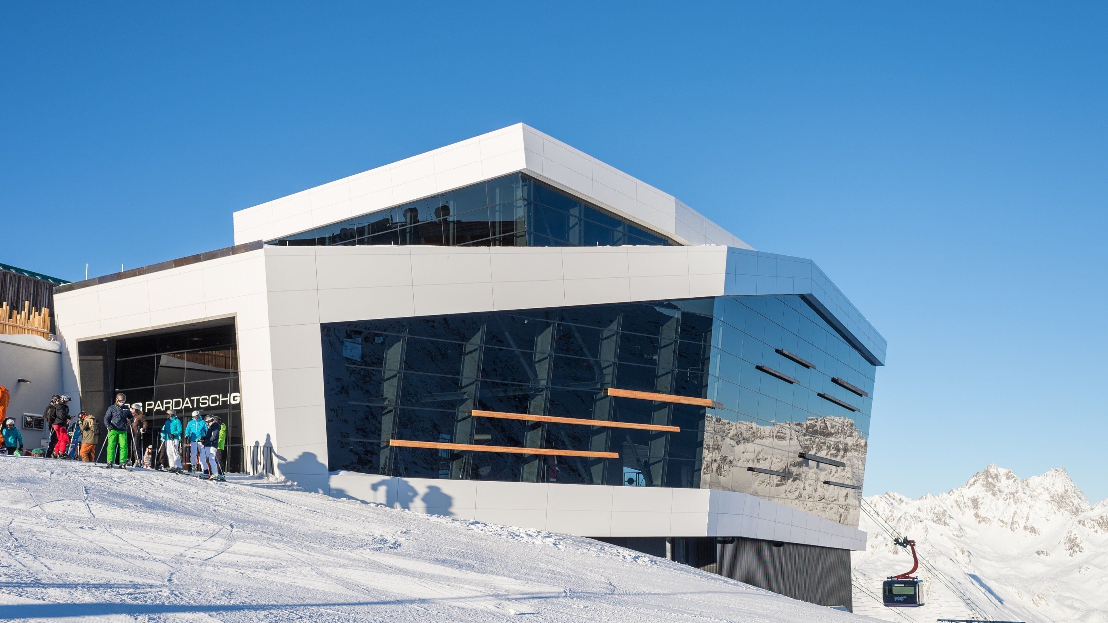 A modern ski resort building with a glass facade and ski lift in the background.