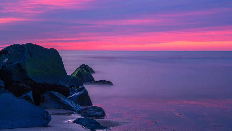 A rocky coastline at sunset with a pink and purple sky.