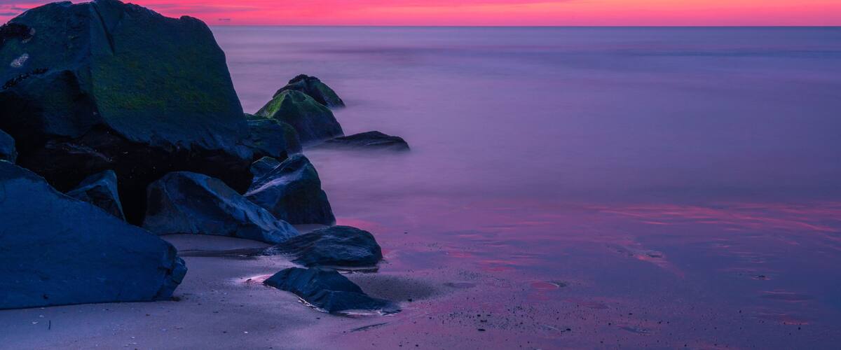 A rocky coastline at sunset with a pink and purple sky.