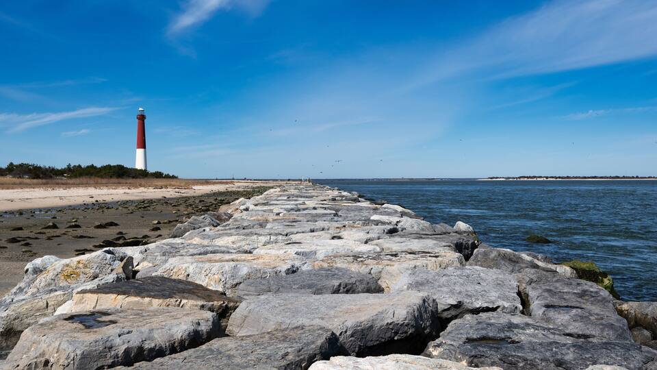 A rocky breakwater leading to a lighthouse on a clear day.