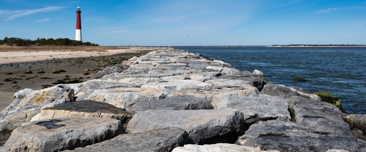 A rocky breakwater leading to a lighthouse on a clear day.