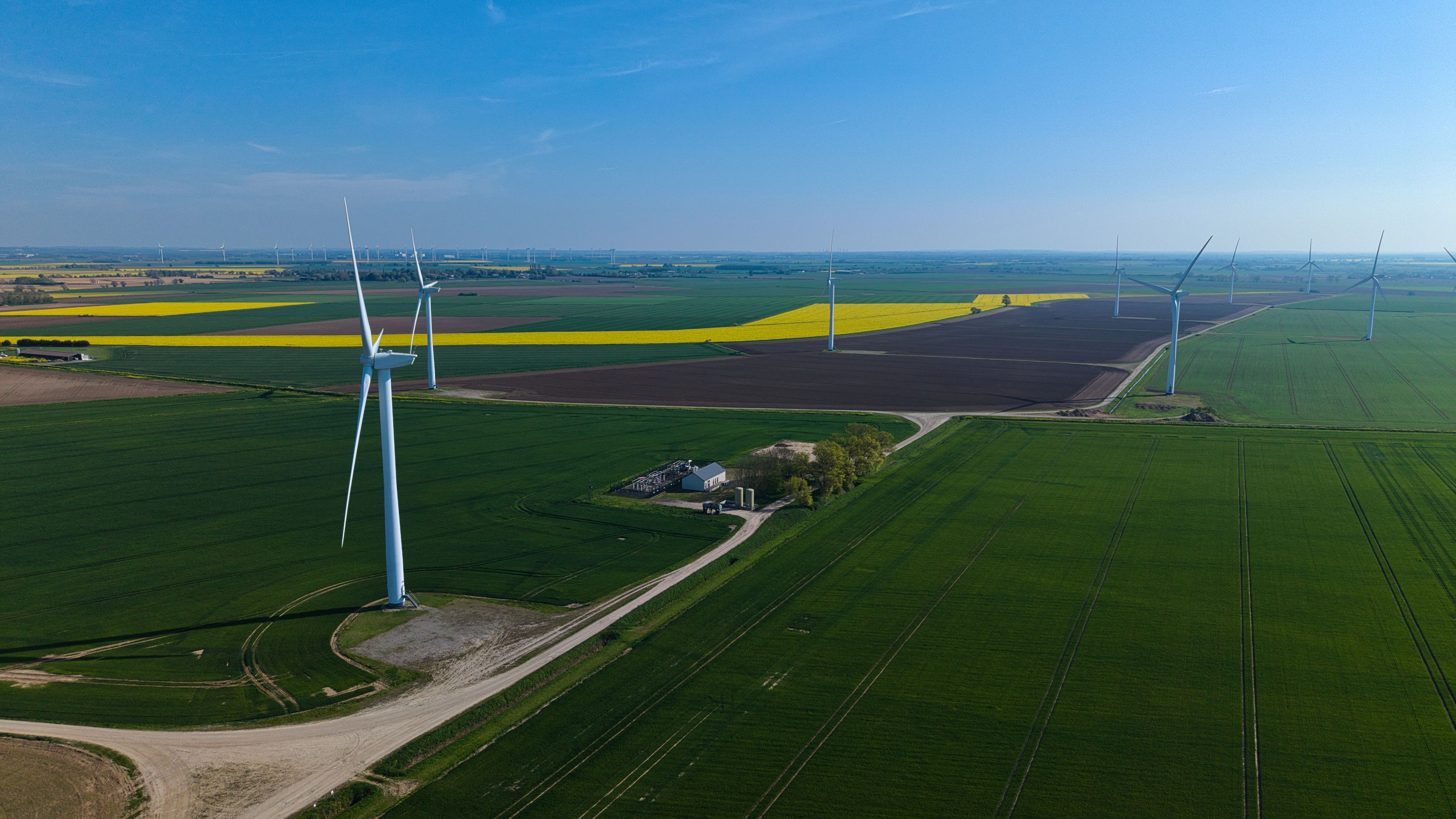 Aerial view of wind turbines standing in green and yellow agricultural fields under a clear blue sky Eastoft, England, United Kingdom.